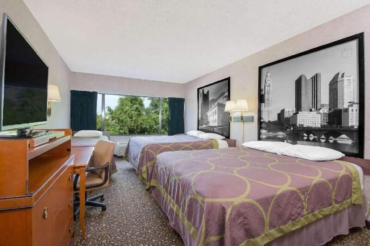 A hotel room with two beds, a desk, a chair, and large windows.