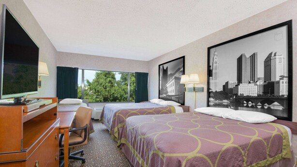 A hotel room with two beds, a desk, a chair, a large window, and a cityscape view.