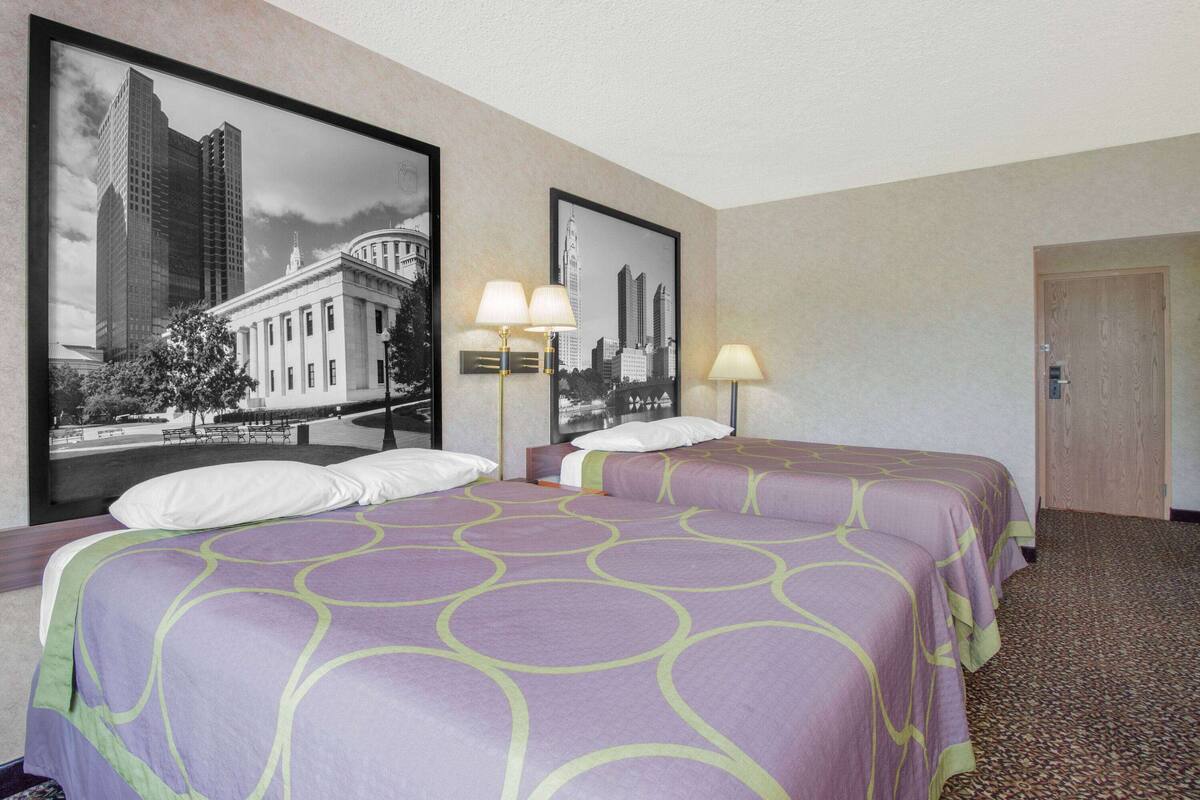 Een hotelkamer met twee bedden, een groot stadsbeeld in een lijst aan de muur en een houten deur.