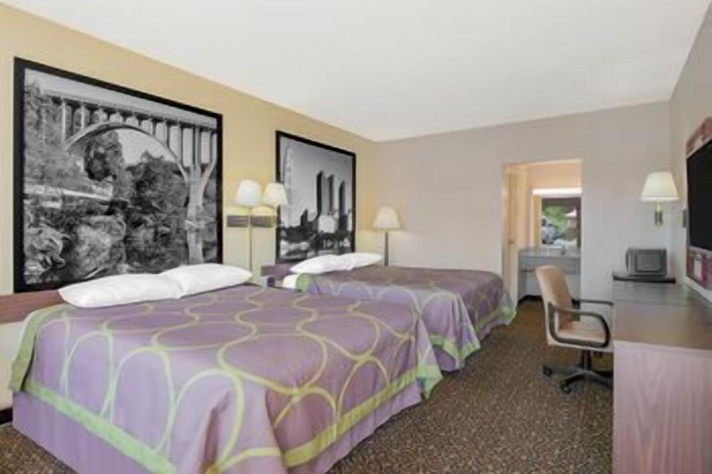 A hotel room with two beds, a desk, a chair, and a television.