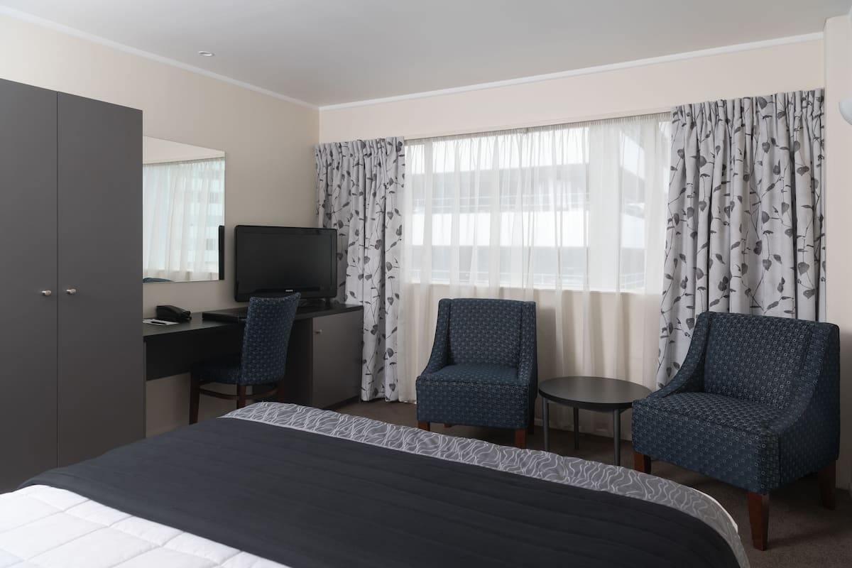 Ein Hotelzimmer mit Bett, Schreibtisch, Stuhl, Fernseher und einem fenster mit Vorhängen.