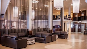 Un hall amplio con sofás de cuero, ventanas grandes con cortinas traslúcidas y un nivel intermedio con una escalera.