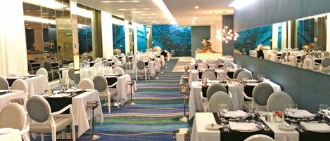 A banquet hall with tables set for dining, a patterned carpet, and large windows.