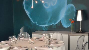 Un comedor con una mesa redonda para seis personas, sillas transparentes, una lámpara moderna y un mural en la pared.