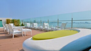 Une terrasse sur le toit, avec des chaises en osier blanches et un fauteuil de détente jaune, d’où l’on peut admirer un plan d’eau et le paysage urbain.