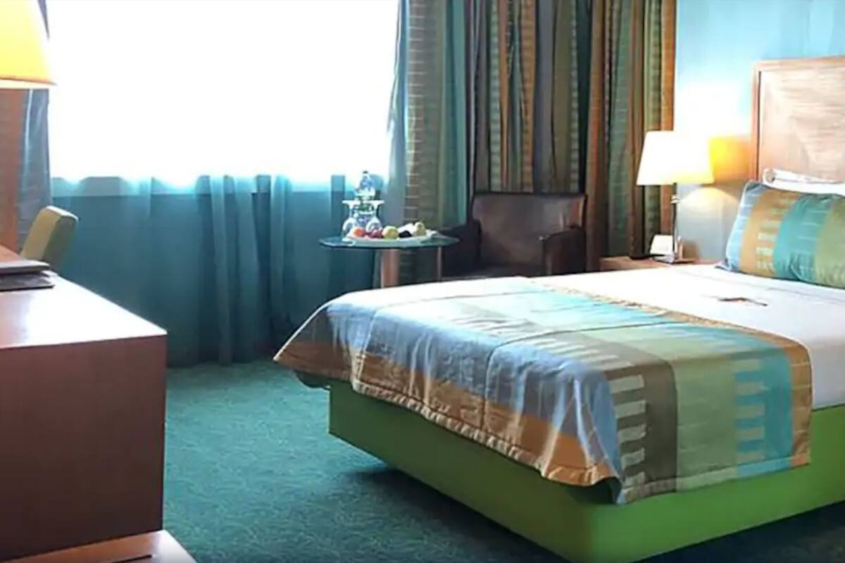 A hotel room with a large bed, a bedside table, a chair, and a small table with a lamp.