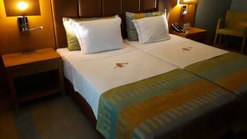 Una cama bien hecha con sábanas blancas y dos almohadas, una mesita de noche con un teléfono y una lámpara de pared.