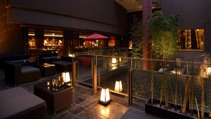 Zona lounge moderna e interna con posti a sedere, un bar e una ringhiera in vetro che si affaccia su un giardino curato.