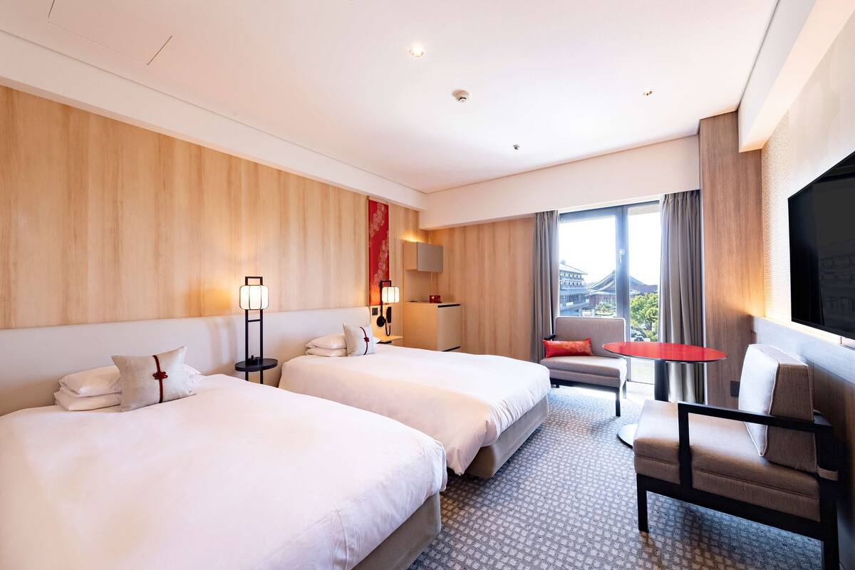 Hotellihuone, jossa on kaksi sänkyä, sohva, pieni pöytä ja televisio.