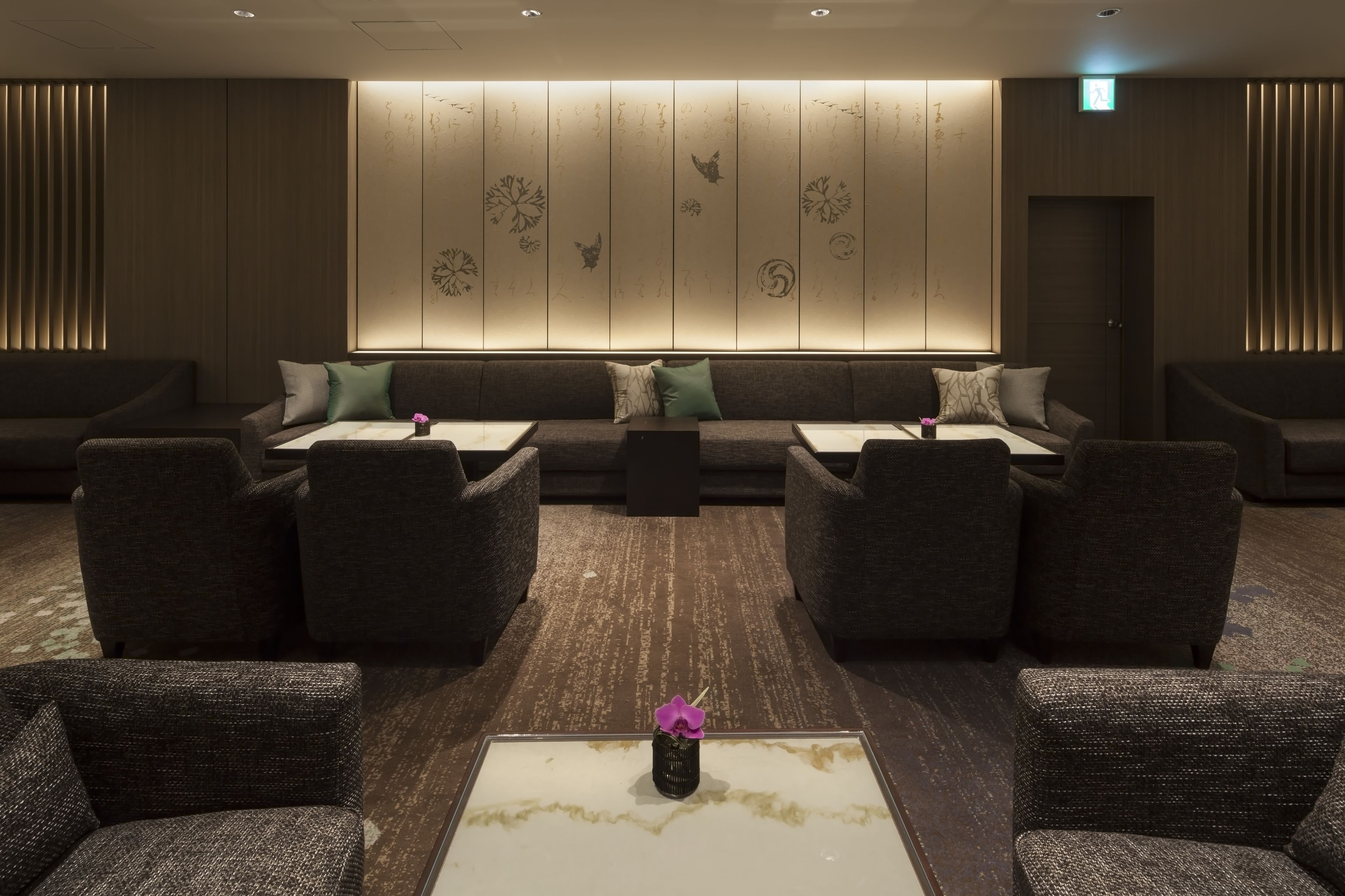 A modern lounge area with sofas and armchairs arranged around a central coffee table, featuring a decorative vase.