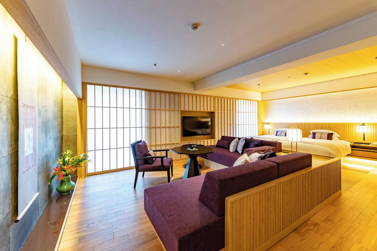Moderni hotellihuone, jossa on suuri sänky, sohva, televisio ja puulattia.