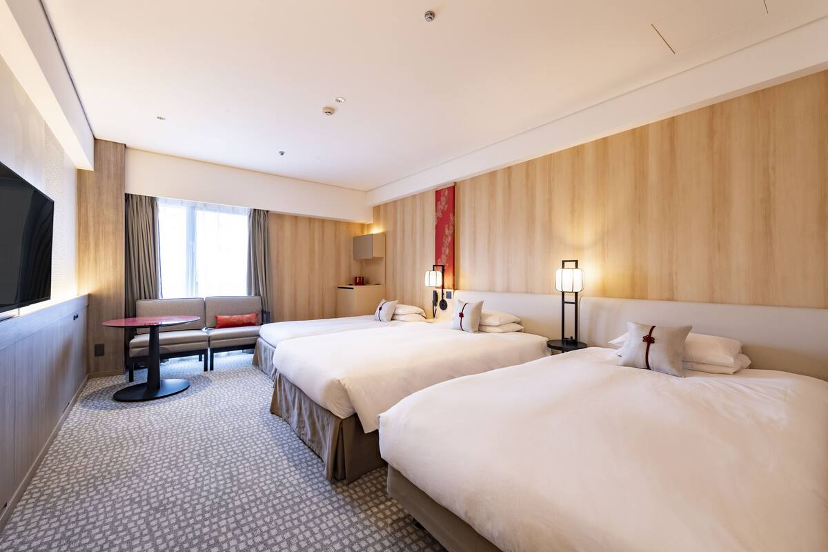 Hotellihuone, jossa on kaksi sänkyä, sohva, pieni pöytä ja televisio.