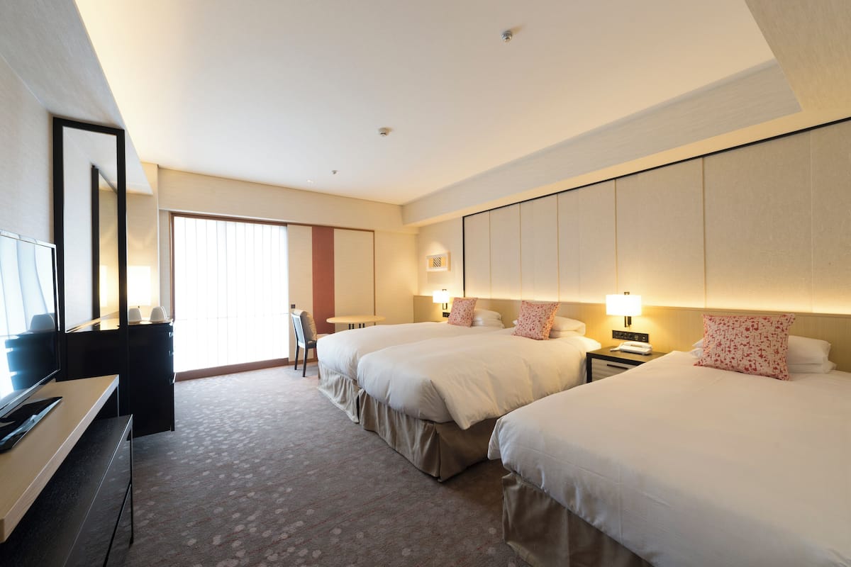 A hotel room with two beds, a desk, a chair, and a television.
