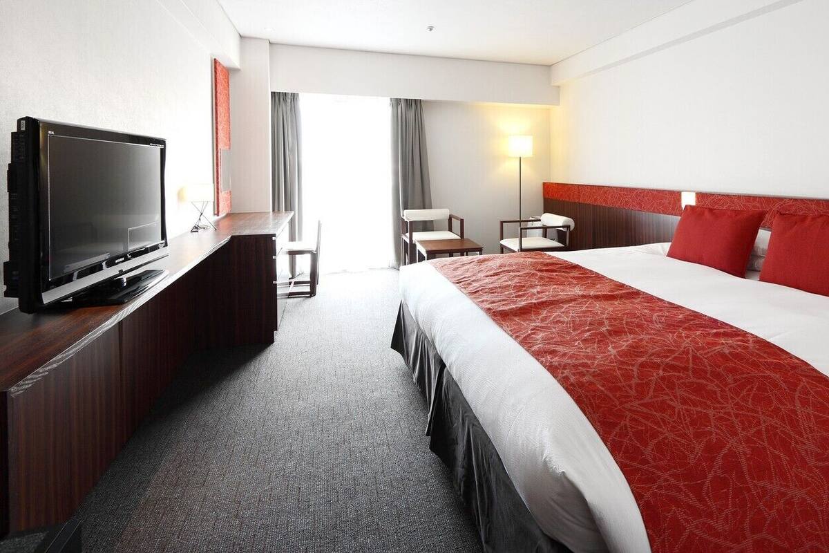 Hotellihuone, jossa on suuri sänky, puinen lipasto, jossa on televisio, työpöytä ja tuoli.