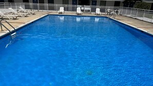 A rectangular swimming pool with clear blue water, surrounded by white lounge chairs and a white fence. - The Nest Hotel Suffolk (Suffolk)