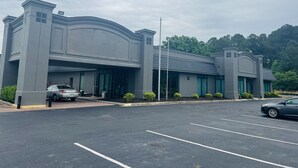 A modern building with a large entrance, parking lot, and a flagpole. - The Nest Hotel Suffolk (Suffolk)