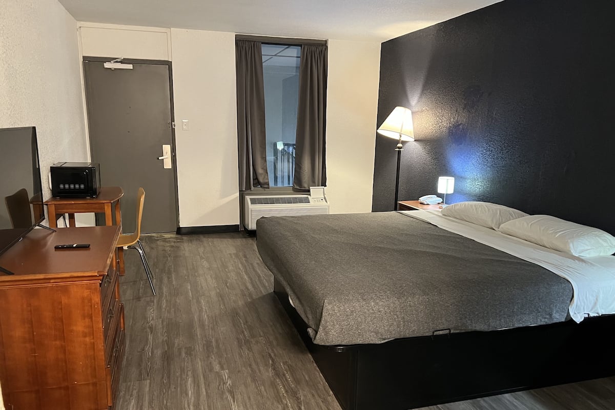 A hotel room with a bed, a desk with a computer, a chair, a lamp, and a window with curtains.
