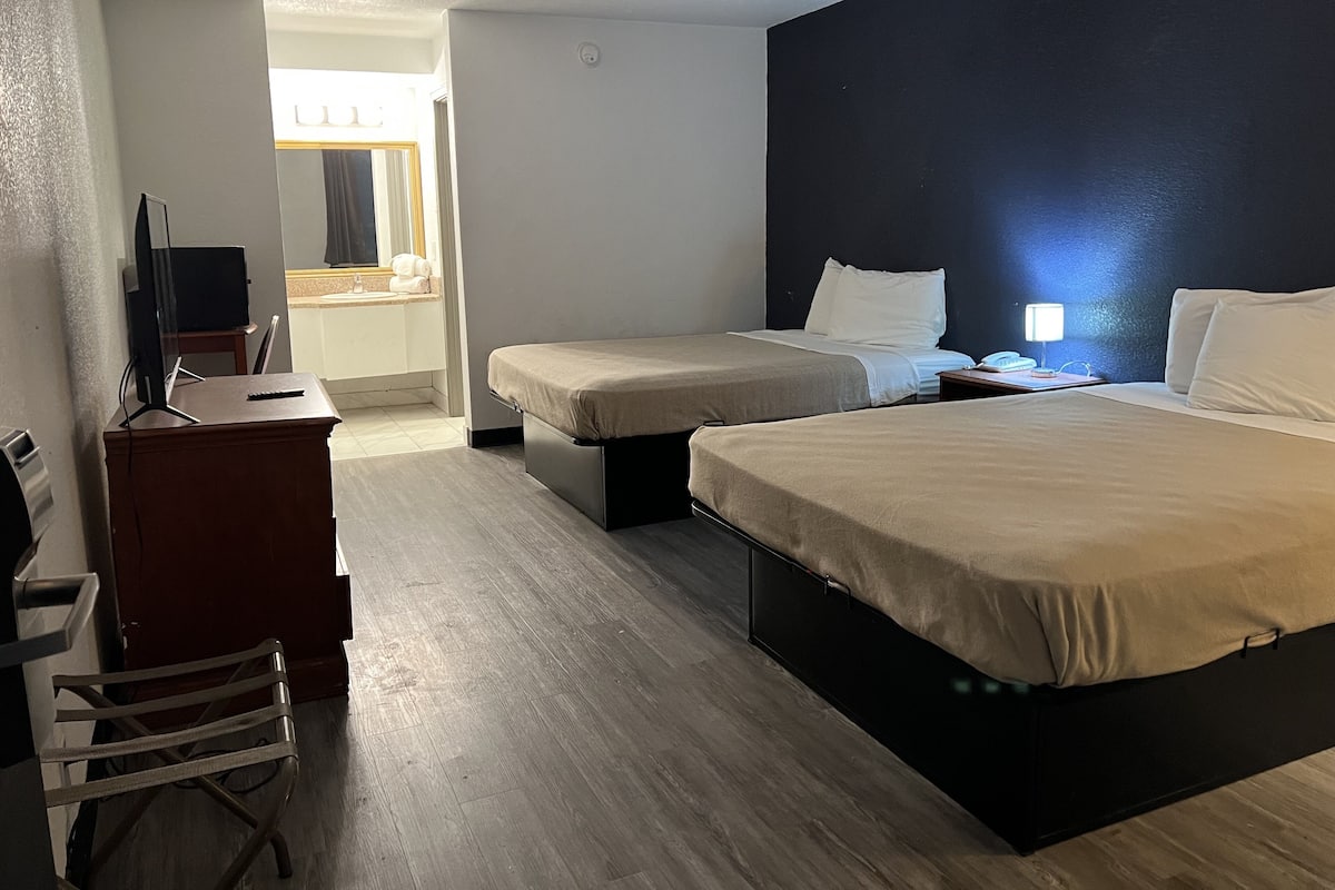 A hotel room with two beds, a desk, a chair, and a TV.