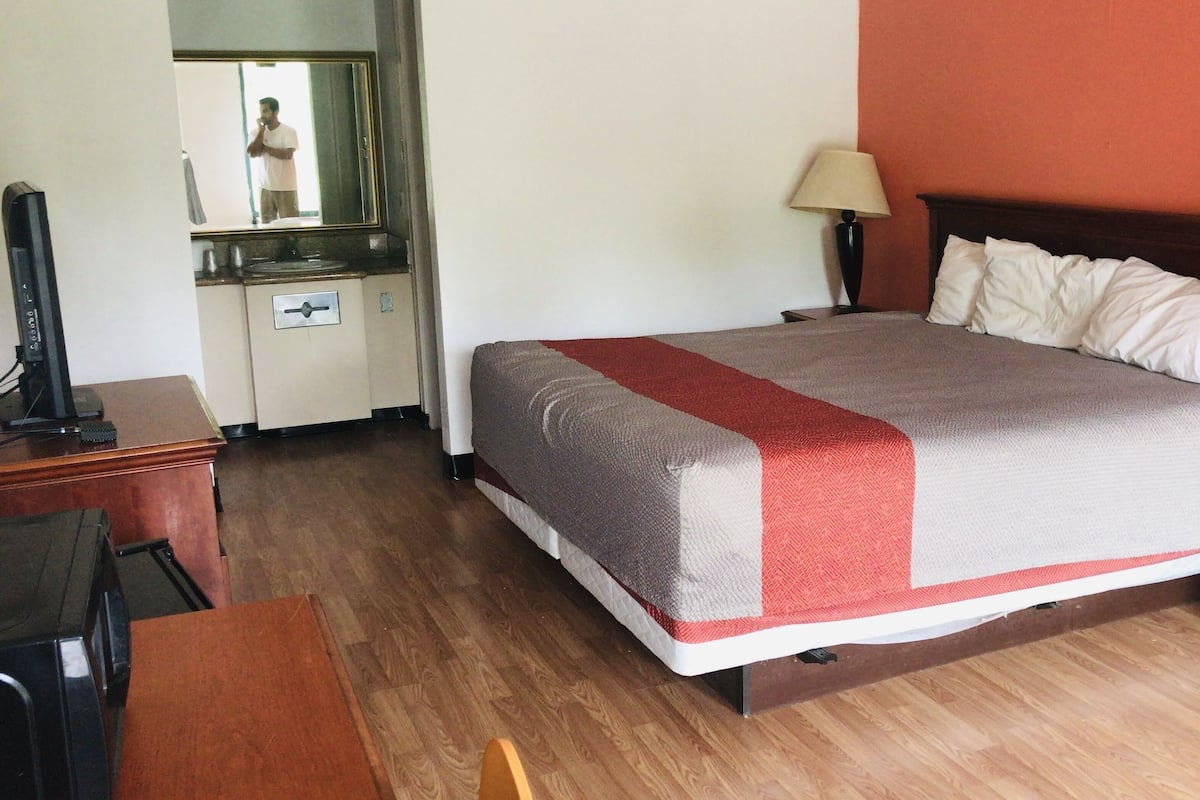 A hotel room with a bed, two bedside lamps, a desk with a computer, and a mirror.
