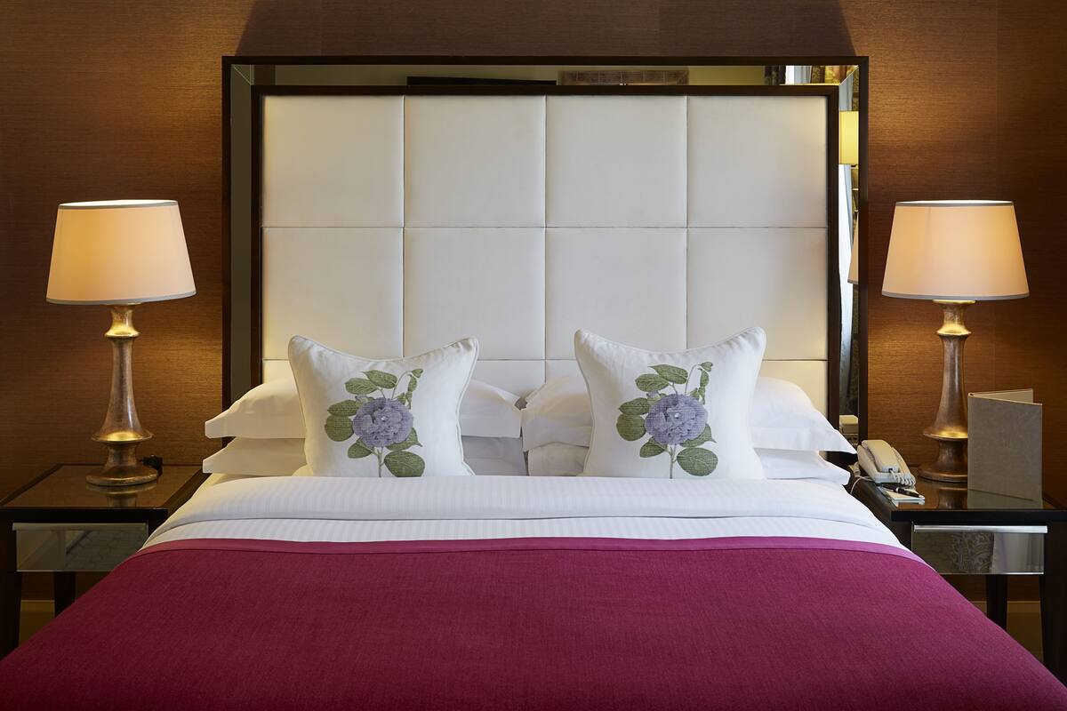 A hotel room with a large bed, two bedside lamps, and a mirror above the bed.