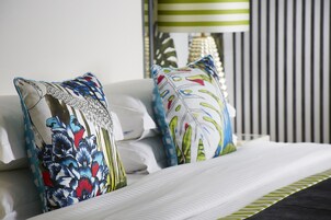 Ein ordentlich gemachtes Bett mit weißen Leinentüchern und dekorativen Kissen mit floralem Muster.