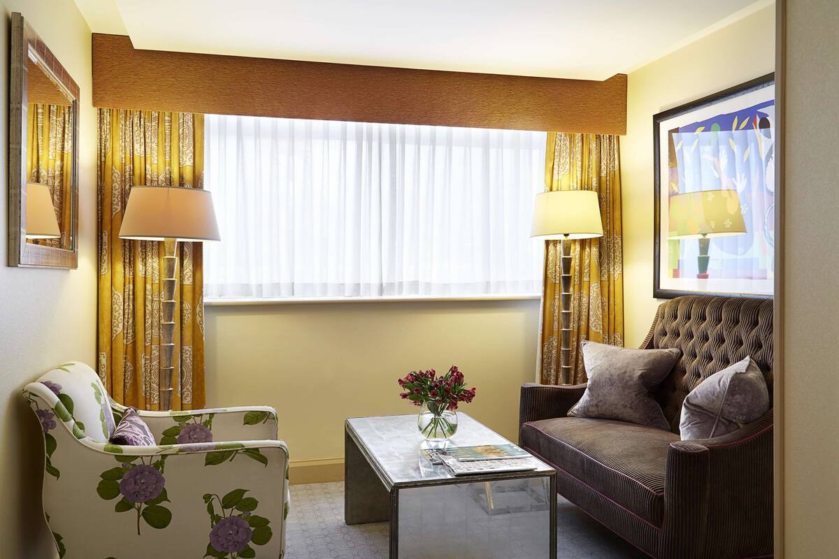 A modern living room with a sofa, armchair, and coffee table. There is a window with curtains, a lamp, and a framed picture on the wall.