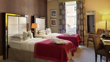 A hotel room with two beds, a desk, a chair, and a window with curtains.
