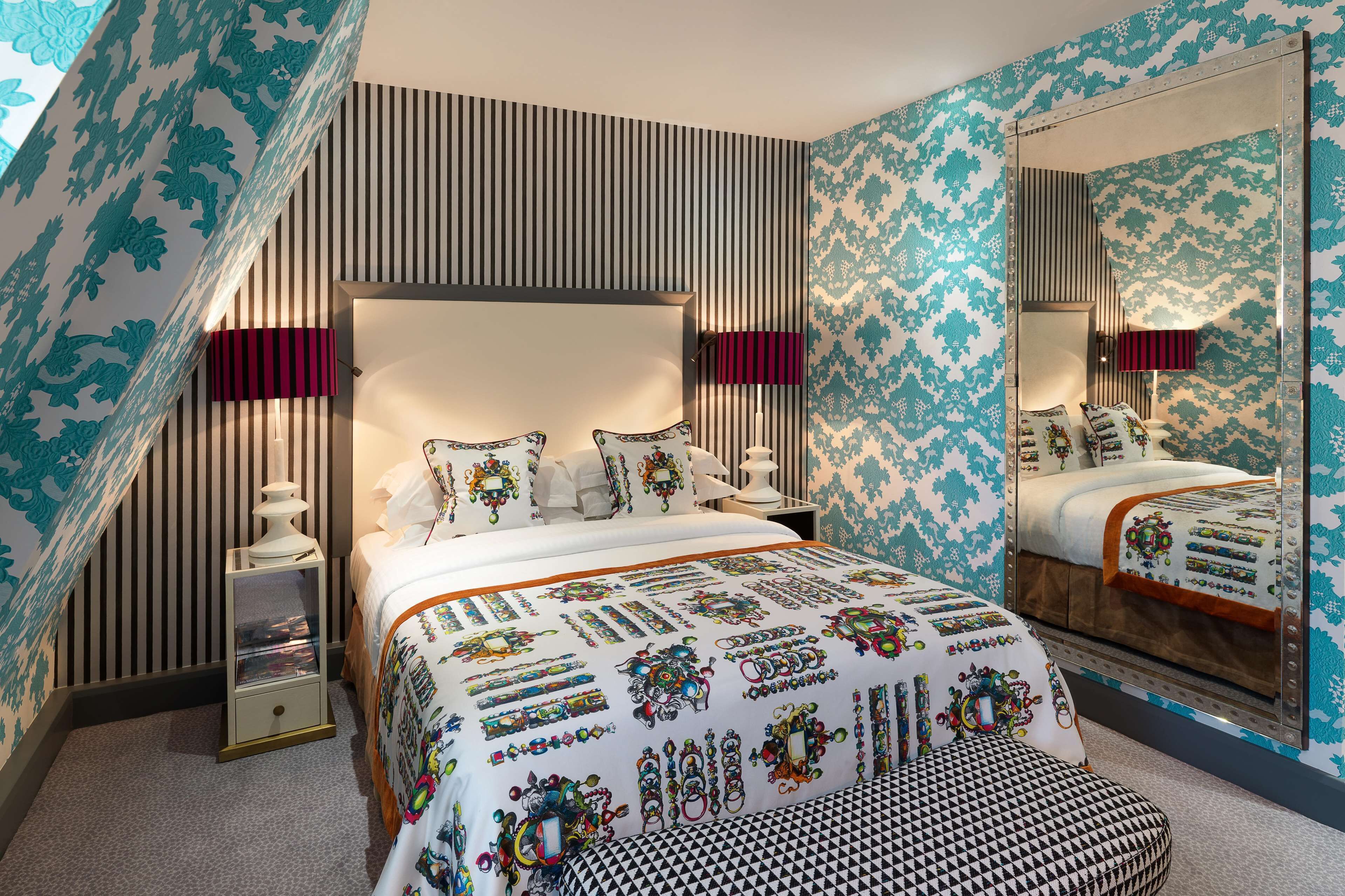 Un dormitorio con una cama grande, una mesita de noche, un espejo y papel tapiz estampado.