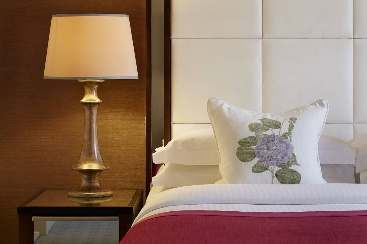 A neatly made bed with a floral pillow, a bedside lamp, and a wooden nightstand.