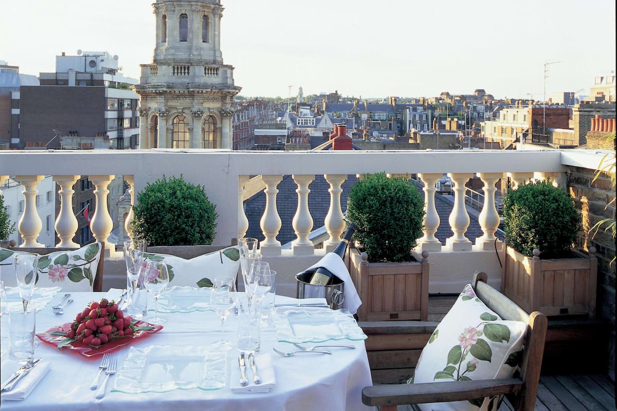 A rooftop dining area with a table set for two, overlooking a cityscape with historic buildings and a prominent tower.