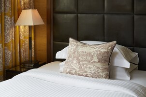 A neatly made bed with a patterned pillow, a bedside lamp, and curtains with a traditional design.
