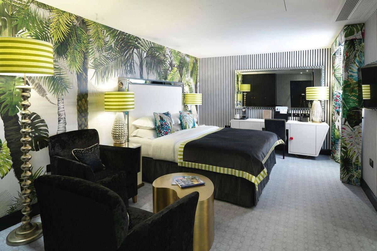 A hotel room with a bed, two chairs, a desk, a television, and a mirror.