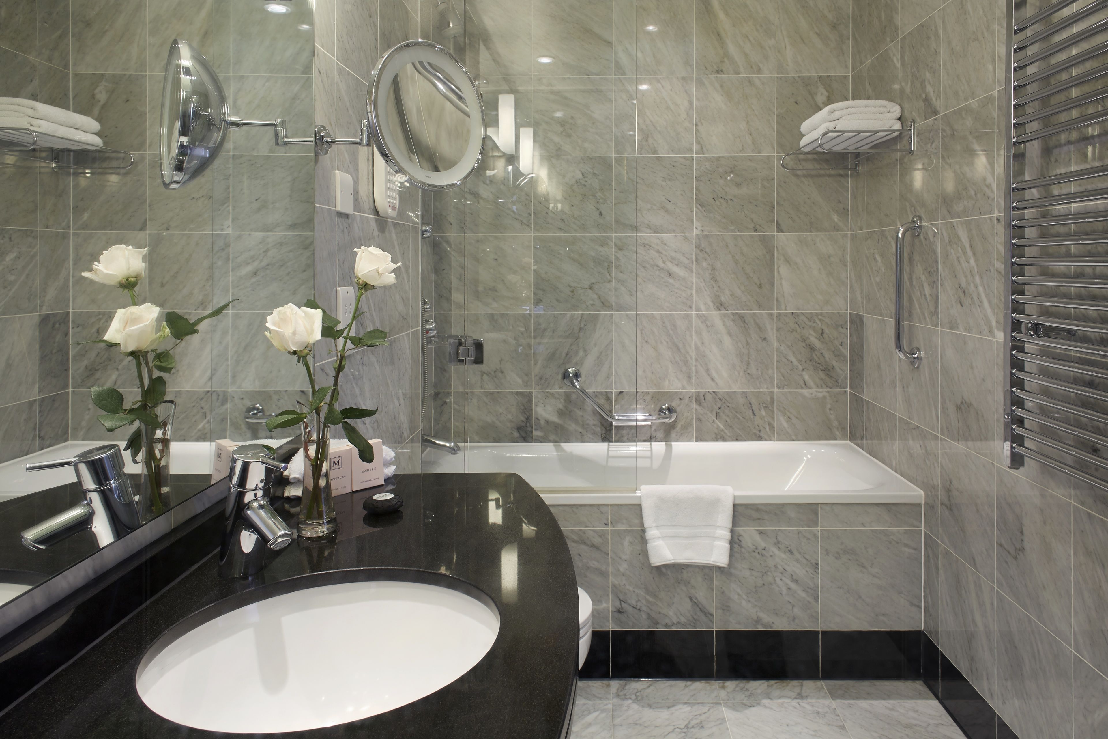 Un baño moderno con un lavabo negro, un espejo grande, una bañera y un perchero para toallas.