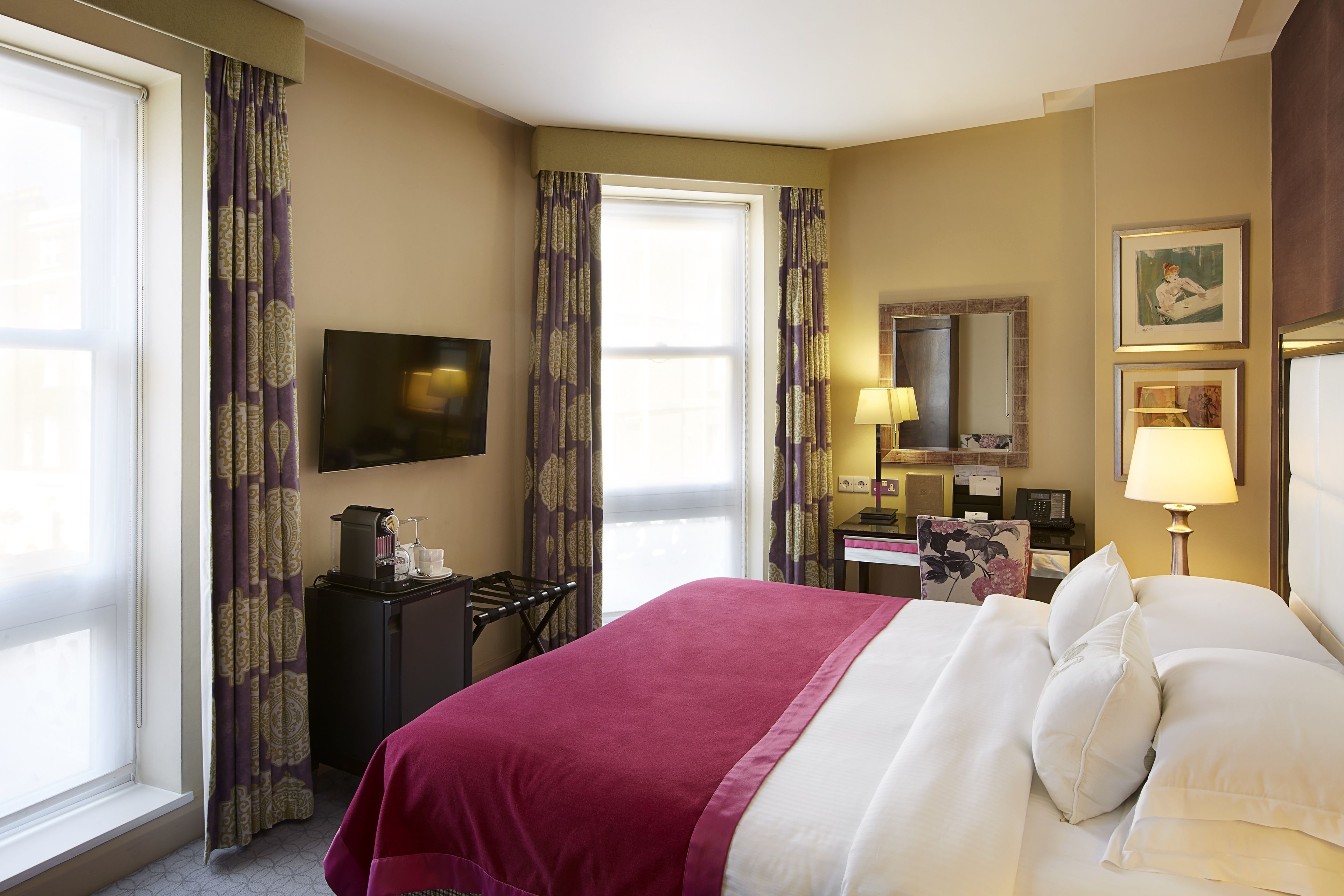 A hotel room with a large bed, a desk, a chair, a television, and a window with curtains.