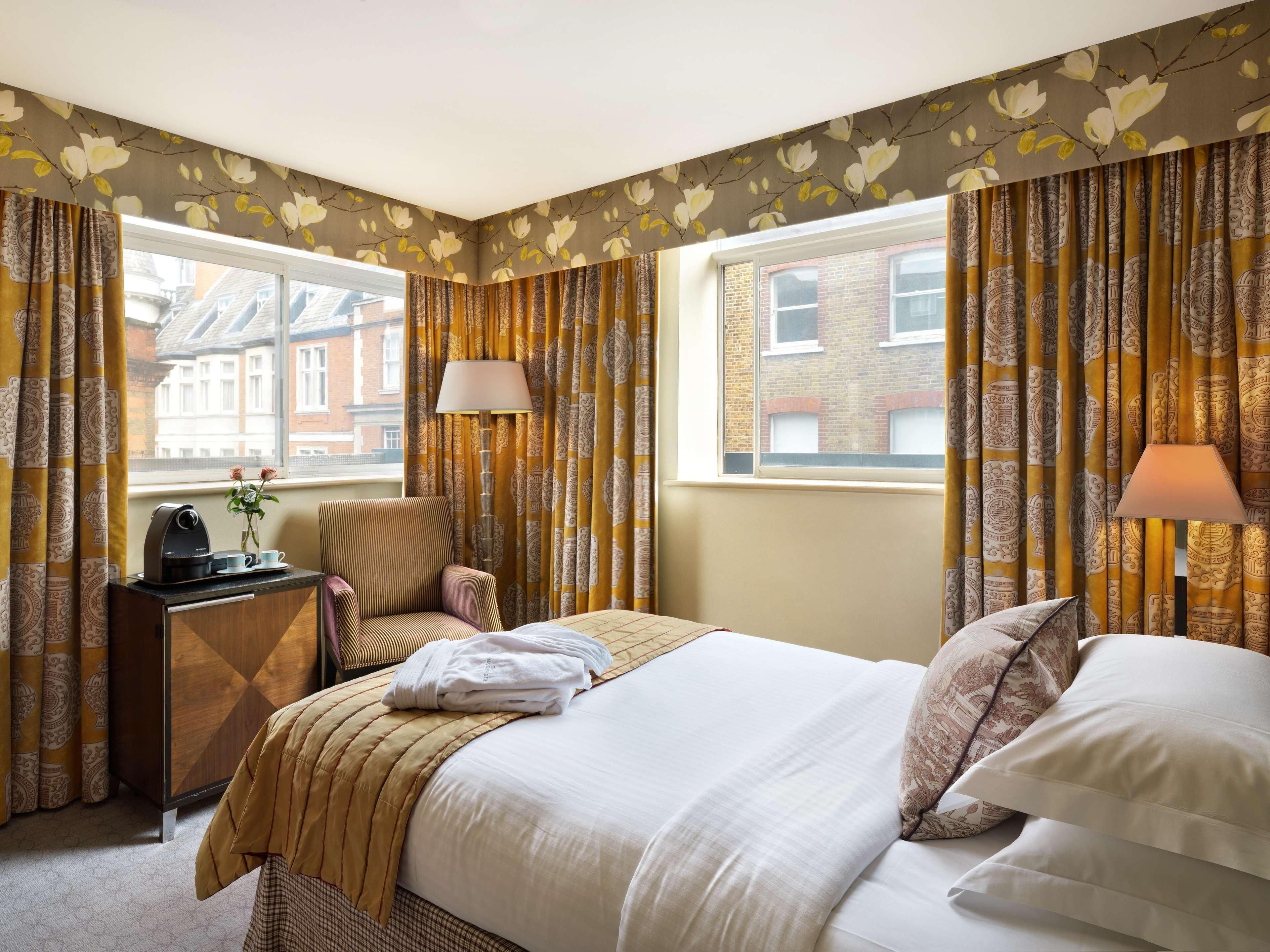 A hotel room with a bed, bedside tables, a chair, a lamp, and curtains.
