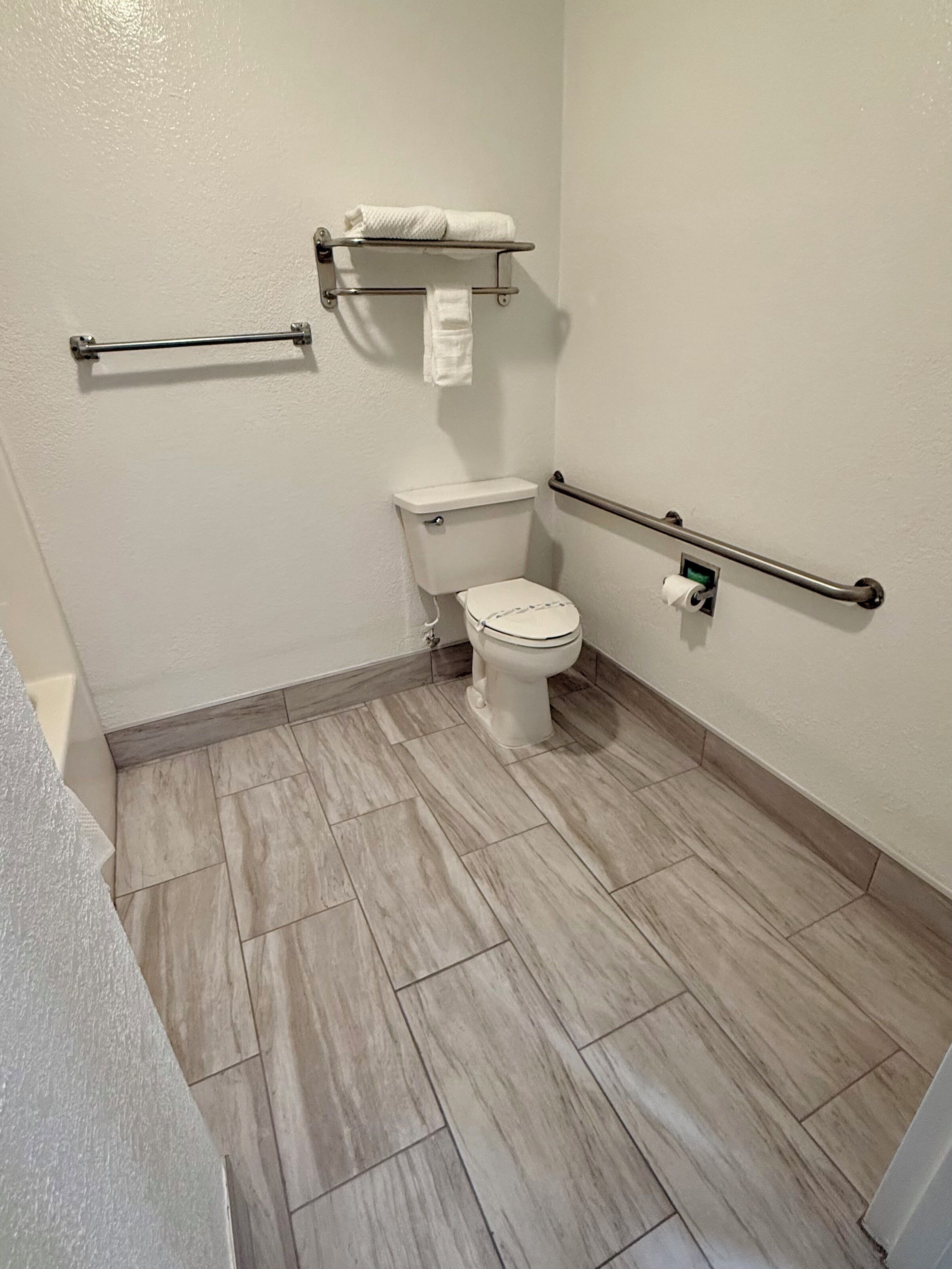 Une salle de bain équipée de toilettes, d’un porte-serviettes et d’une barre d’appui.