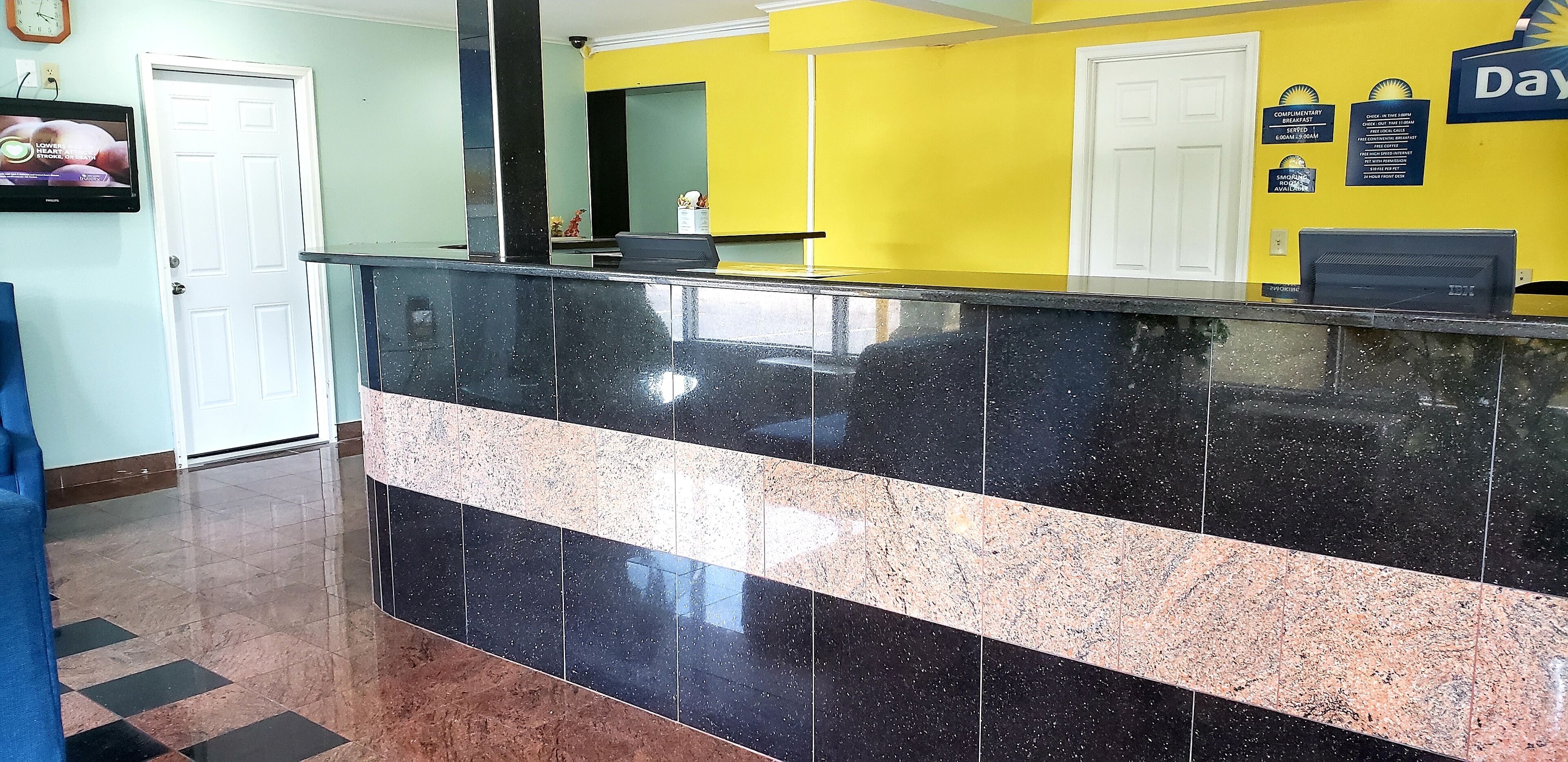 Una recepción con mostrador de mármol negro, pared amarilla y puerta blanca.