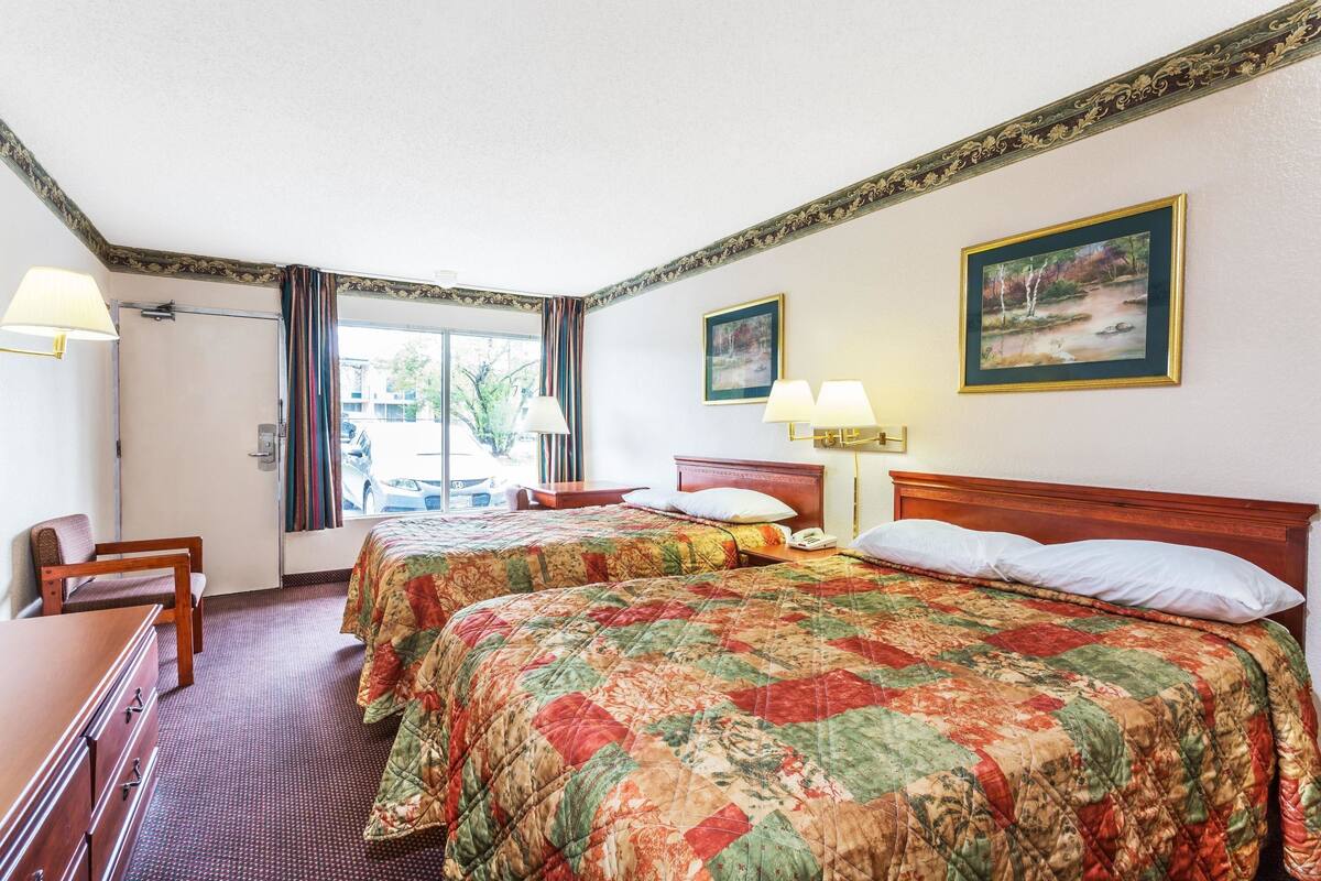 A hotel room with two beds, a desk, a chair, and a window with curtains.