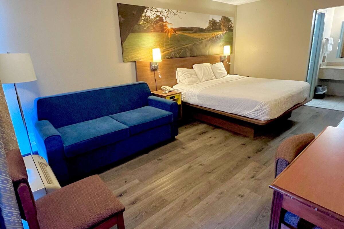A hotel room with a bed, a blue sofa, a wooden floor, and a painting on the wall.