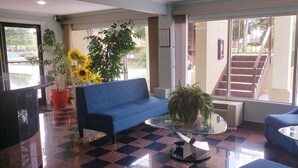 Un hall d’entrée avec un canapé bleu, une table basse en verre, des plantes en pot et un escalier menant à un étage supérieur.