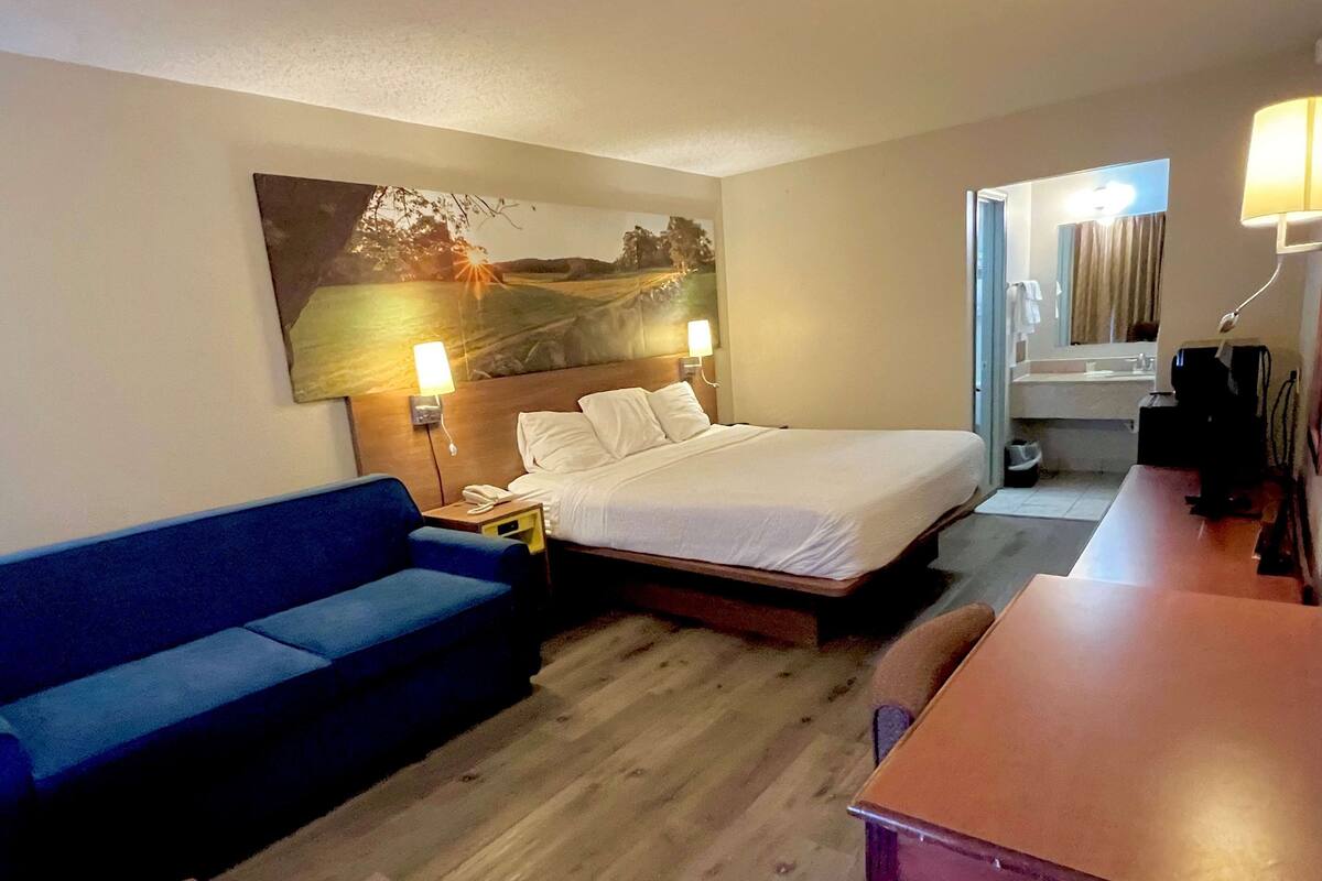 A hotel room with a bed, a blue sofa, a wooden table, and a painting on the wall.