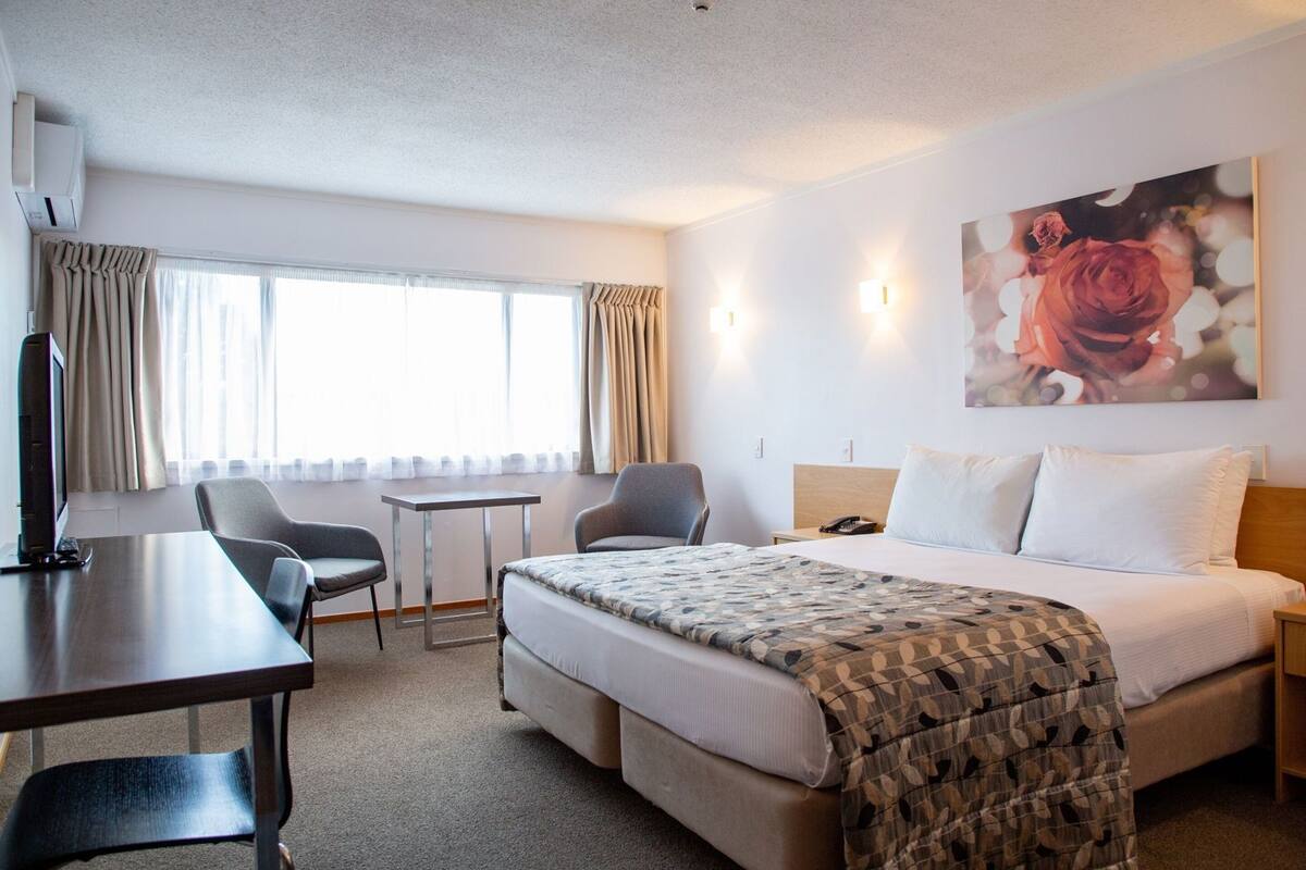 A hotel room with a bed, a desk, two chairs, a small table, and a painting on the wall.