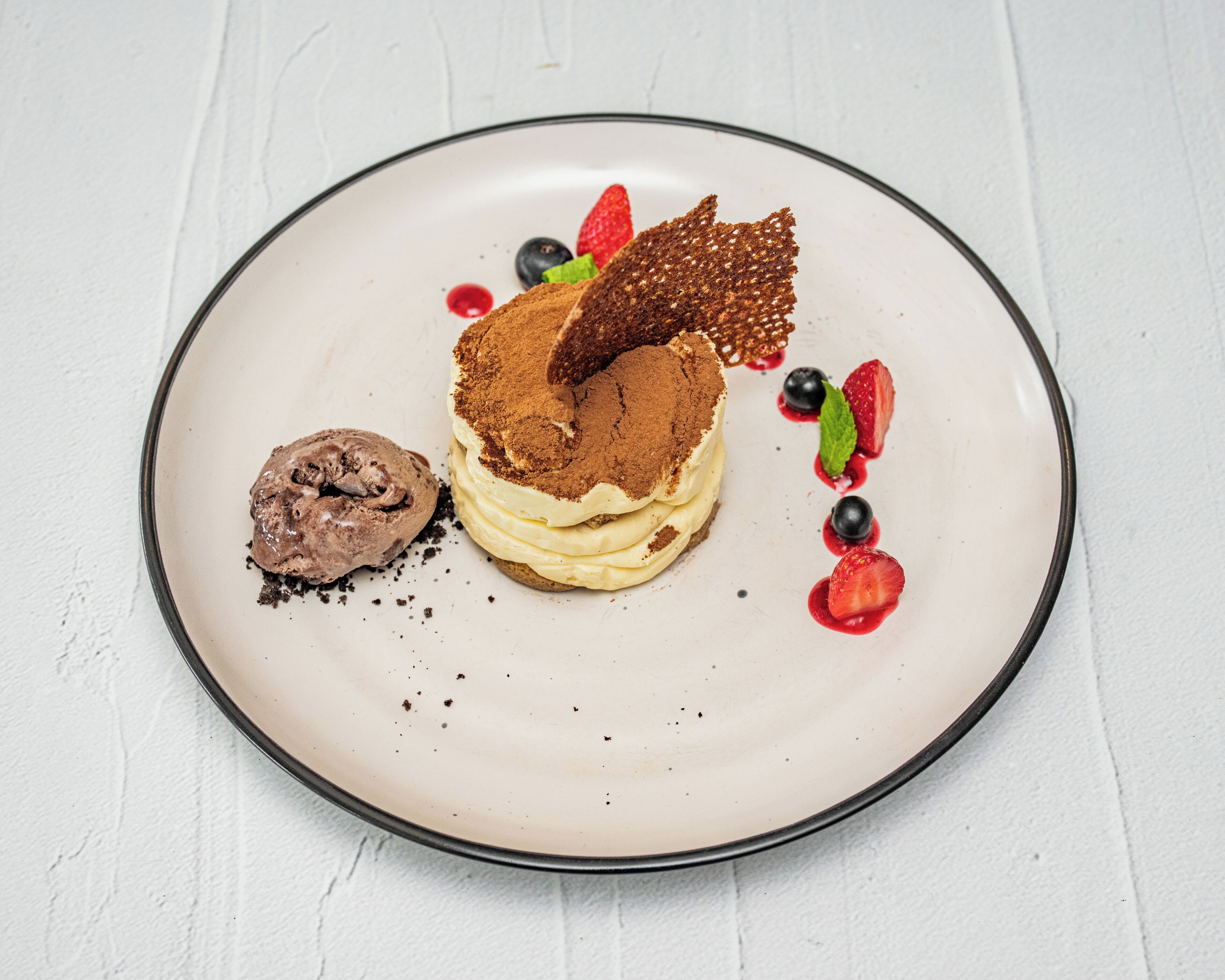 Ein Dessertteller mit einer mehrschichtigen Torte, Schokoladeneis und Beeren.