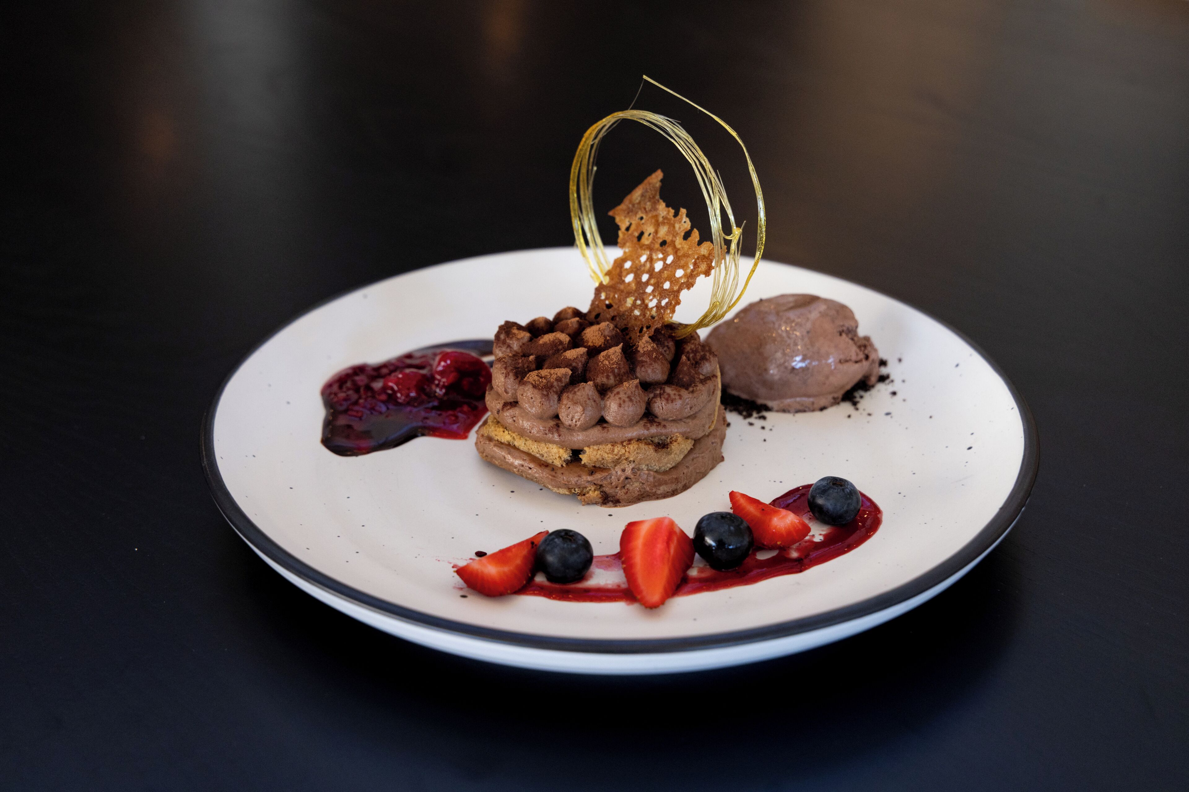 Un plat de postres amb un pastís en capes, baies i una peça de sucre decorativa.
