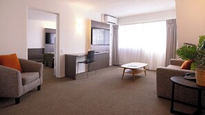A modern living room with a sofa, a dining table, and a kitchen area with a TV. - Auckland Rose Park Hotel (Auckland)