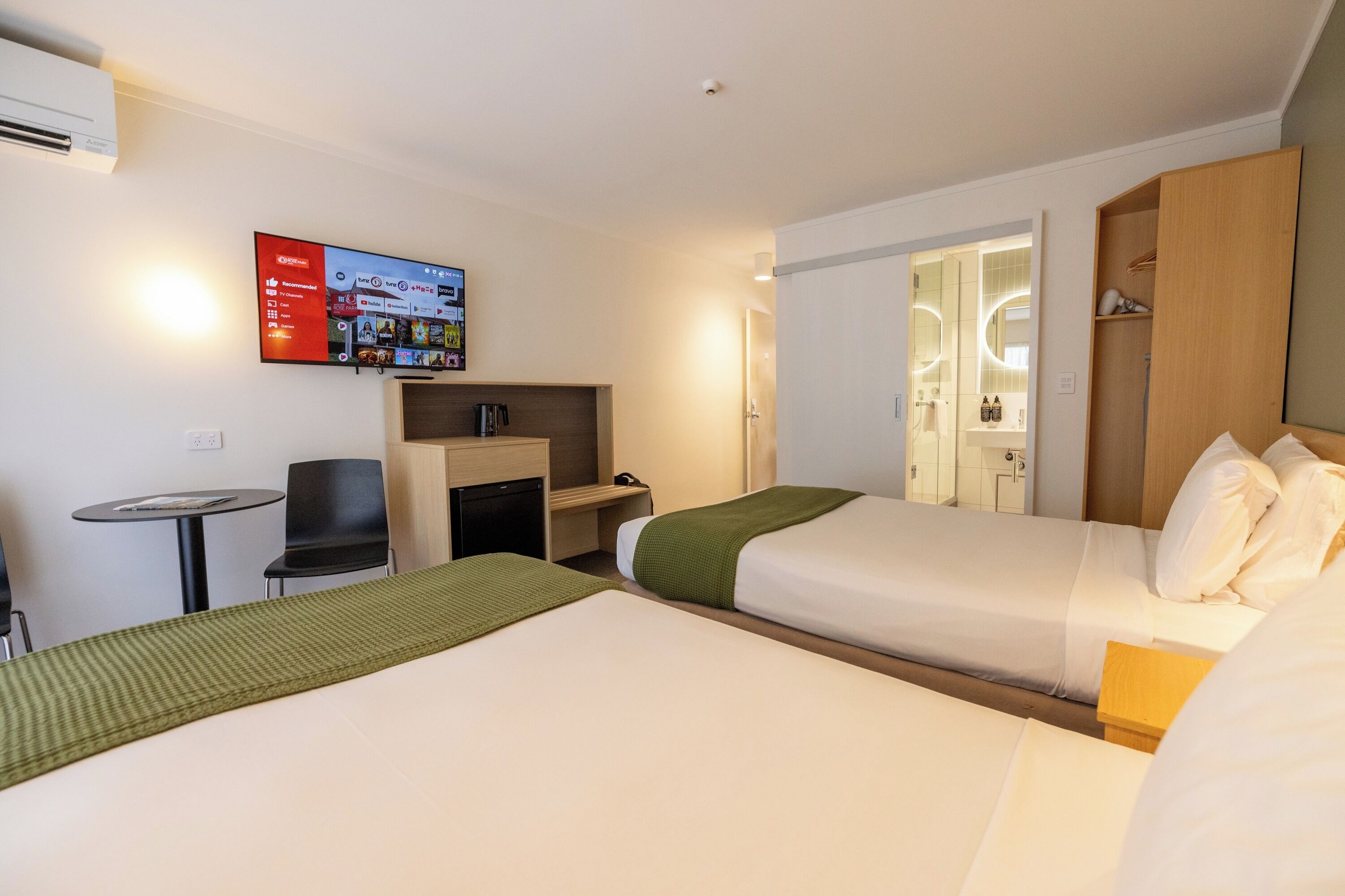 A hotel room with two beds, a TV mounted on the wall, a small table, and a chair.