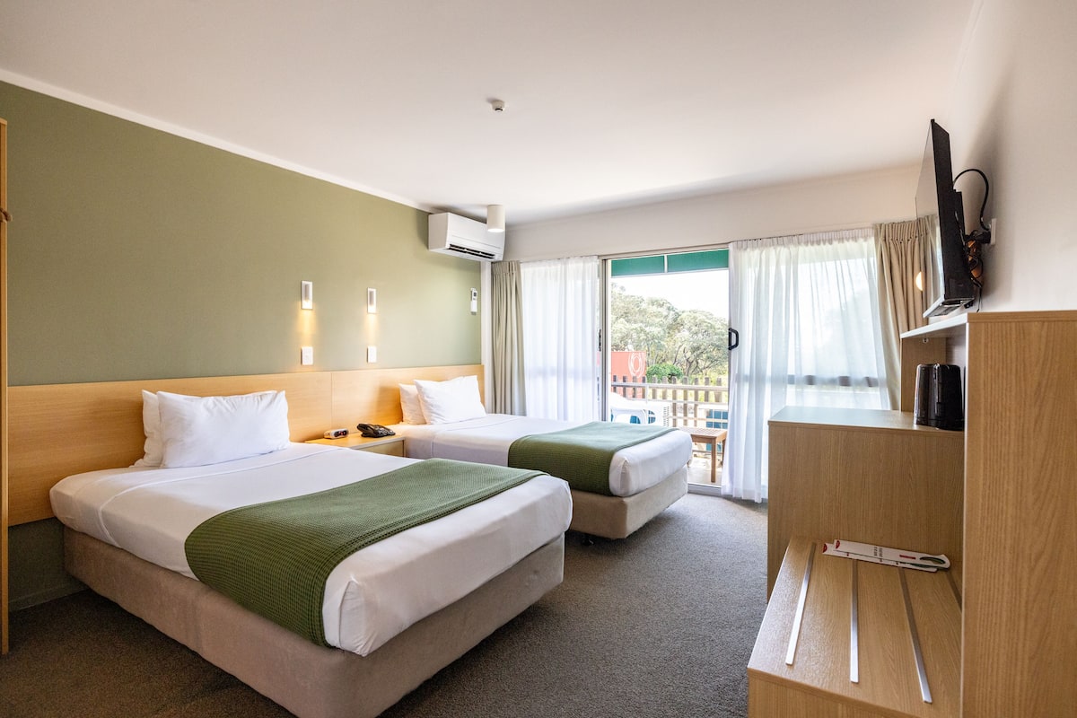 A hotel room with two beds, a TV, and a balcony with curtains.