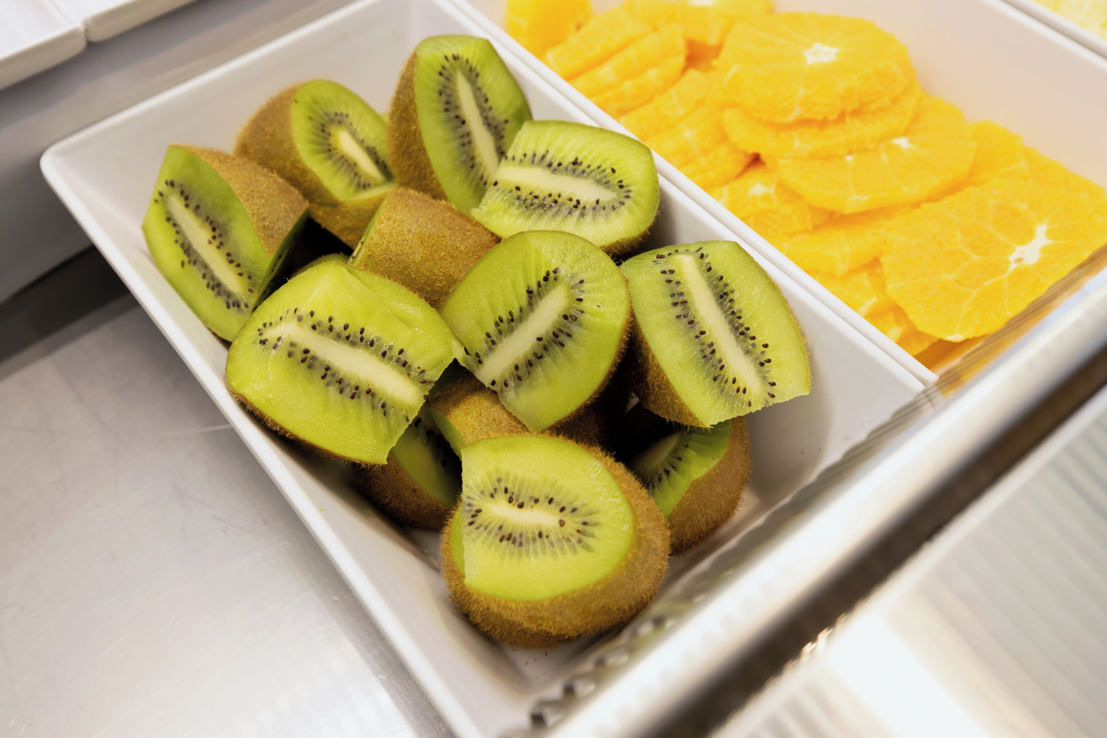 A white tray containing sliced kiwi and orange segments.