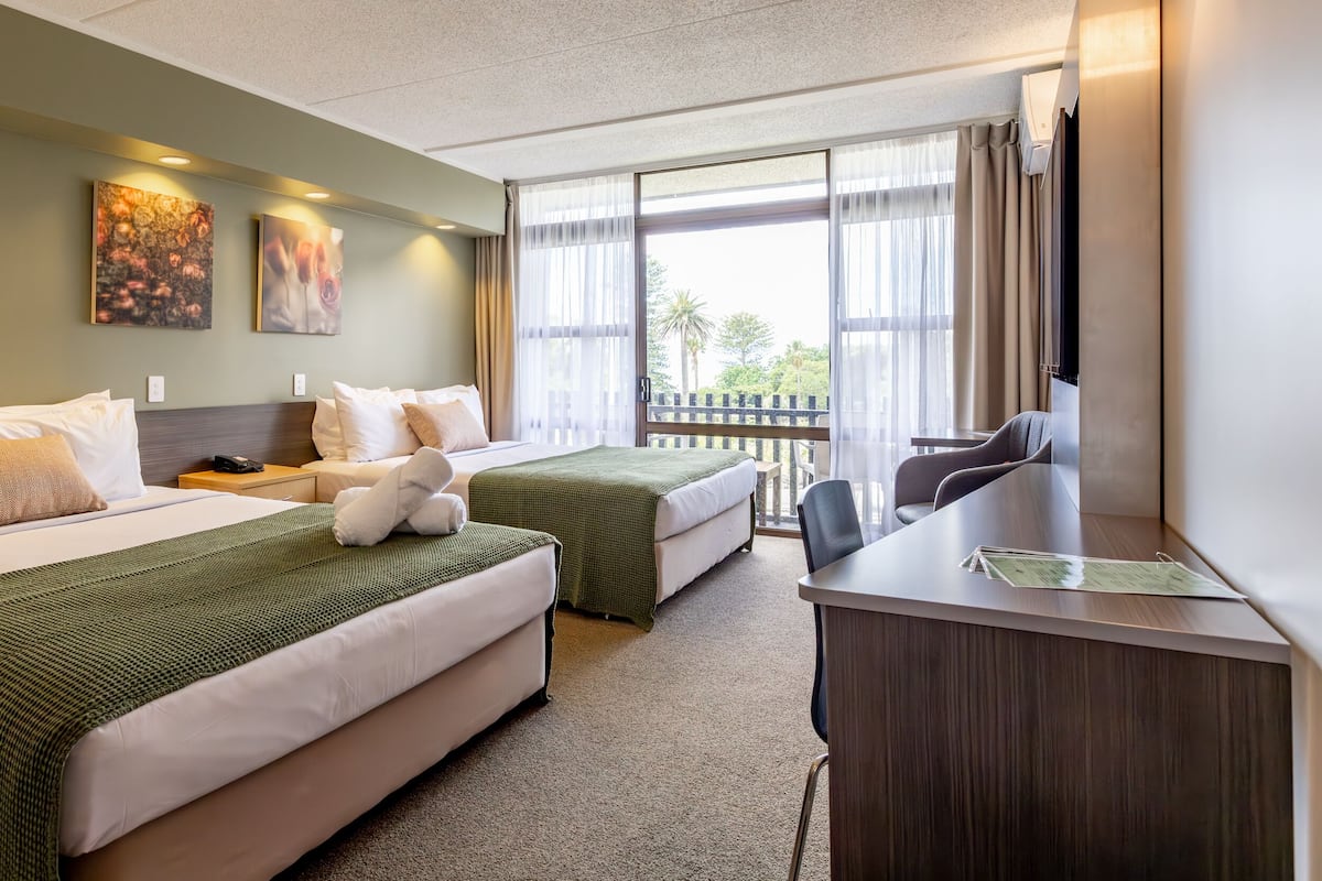 A hotel room with two beds, a desk, and a balcony with a view.