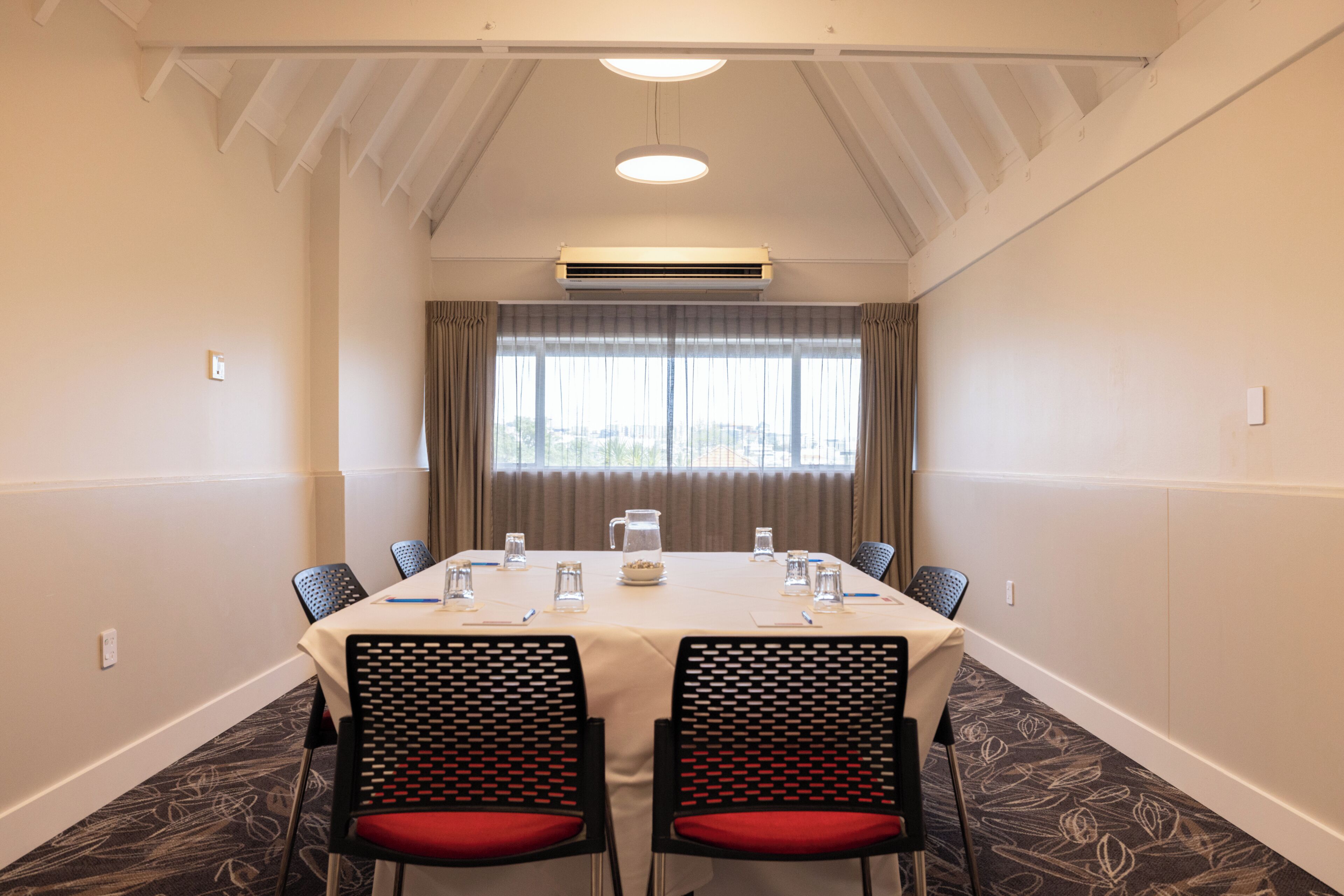 Un salón de conferencias con una mesa, sillas y un ventanal con cortinas.